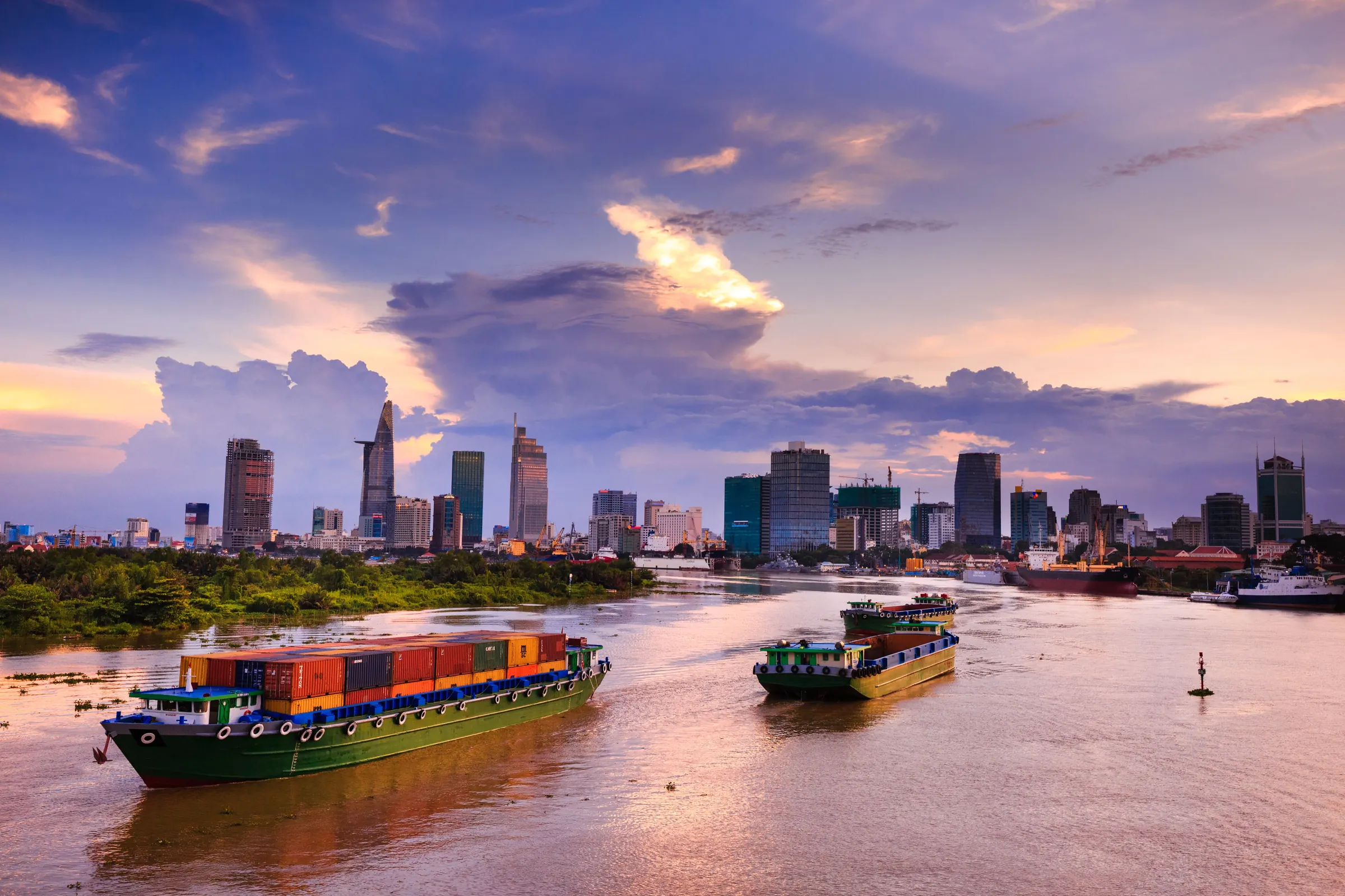 Sà lan chở container trên sông Sài Gòn lúc hoàng hôn, phía sau là trung tâm TP. Hồ Chí Minh